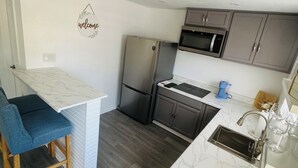 A compact kitchen with a marble countertop, a built-in stove, a refrigerator, and dark wooden cabinets.