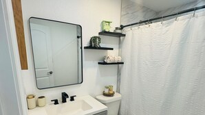 A bathroom with a white sink, mirror, toilet, and shower curtain.