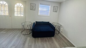 A room with a dark blue sofa, two hexagonal side tables, a window with blinds, and a door.