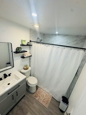 Une salle de bain avec des toilettes blanches, un lavabo, un miroir et un rideau de douche.