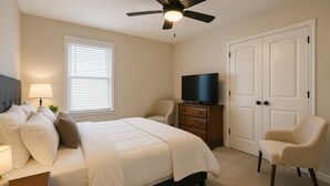 Een slaapkamer met een bed, een televisie op een dressoir, een stoel en een plafondventilator.
