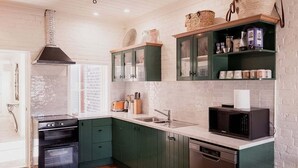 A kitchen with green cabinets, a black stove, a microwave, and a dishwasher. - The Old Woolstore (Northern Midlands)