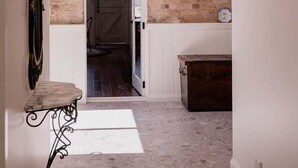 A hallway with a brick wall, a door leading to a room, a small table, and a cabinet. - The Old Woolstore (Northern Midlands)