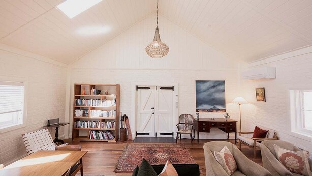 A cozy living room with a high ceiling, a wooden bookshelf, a desk, and a comfortable seating area. - The Old Woolstore (Northern Midlands)