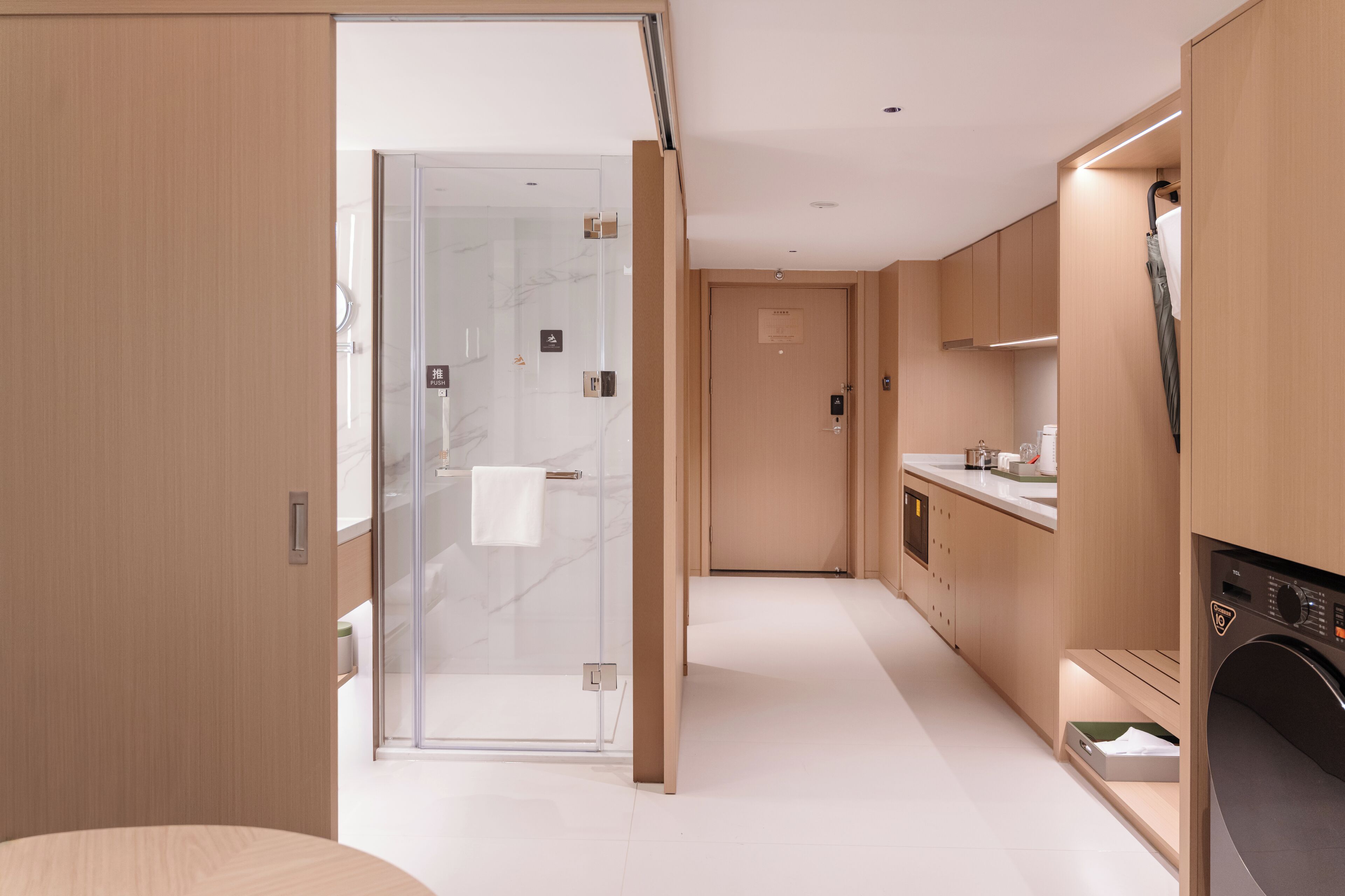 A modern hotel bathroom with a glass shower enclosure, a built-in washing machine, and a minimalist design.