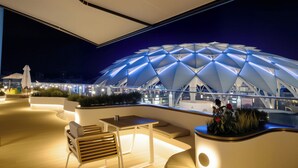 Un espace extérieur aménagé avec un mobilier moderne, comprenant une table et des chaises, et offrant une vue sur une grande structure en forme de dôme illuminée en arrière-plan.