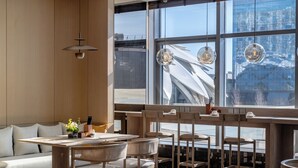 A modern interior with a wooden dining area, cushioned seating, and large windows offering a view of the cityscape. - Beijing XuanLi Hotel (Beijing)