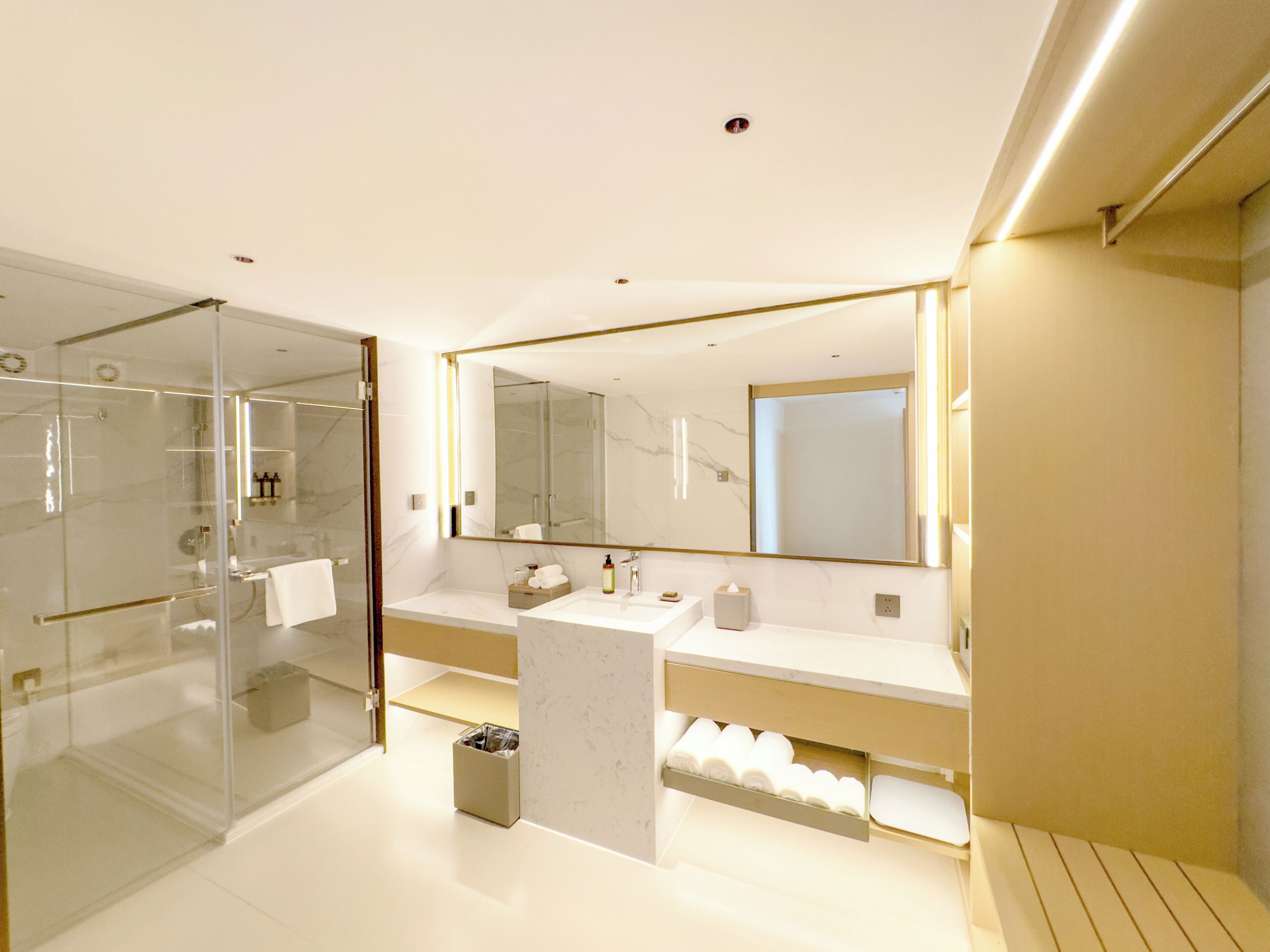 A modern bathroom with a glass shower enclosure, a large mirror, and a marble countertop.
