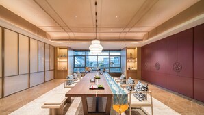 Une salle de conférence spacieuse, dotée d’une longue table, de chaises et d’un lustre moderne.