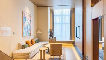 A modern hotel room with a sofa, a small round table, a chair, a TV, and a large window with curtains.