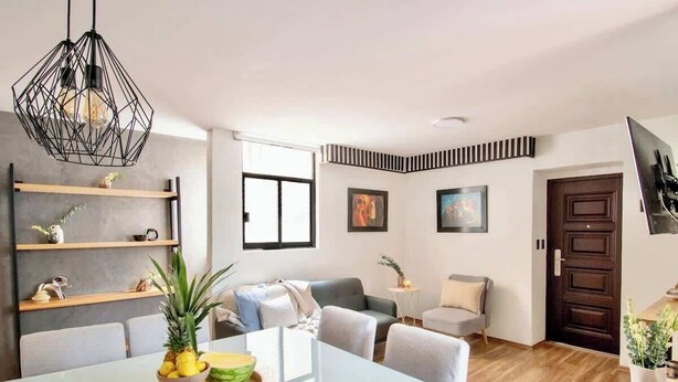 Ein modernes Wohnzimmer mit Essbereich, einer Couch, einem Couchtisch und einer Küchenzeile mit Regalen und einer Pendelleuchte.
