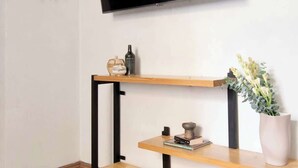 Ein modernes Wohnzimmer mit einem an der Wand montierten Fernseher, Holzregalen und einer Zimmerpflanze.