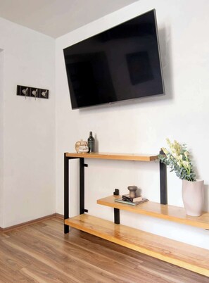 Un salon moderne avec un téléviseur fixé au mur, des étagères en bois et une plante en pot.