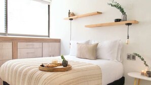 Ein Schlafzimmer mit Bett, Holzboden, Fenster und Nachttisch mit Lampe.