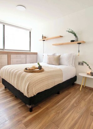 Une chambre à coucher avec un lit, un plancher en bois, une fenêtre et une table de chevet avec une lampe.