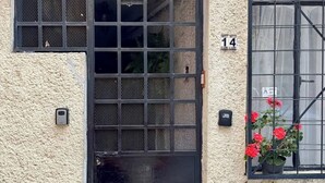 Eine Fassade mit strukturierter Oberfläche, einem schwarzen Metallgitter, einer nummerierten Tür und einem Fenster mit Metallgitter.