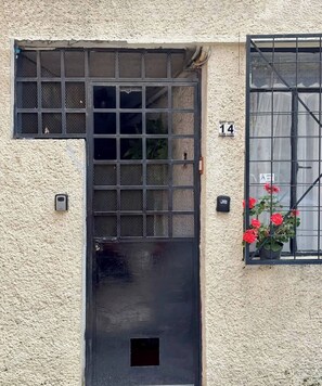 Une façade d’immeuble à l’aspect texturé, agrémentée d’un portail en métal noir, d’une porte numérotée et d’une fenêtre avec une grille en métal.