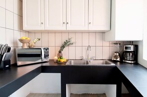 Une cuisine moderne avec des meubles blancs, un plan de travail noir, un évier encastré, une machine à café et un four à micro-ondes.