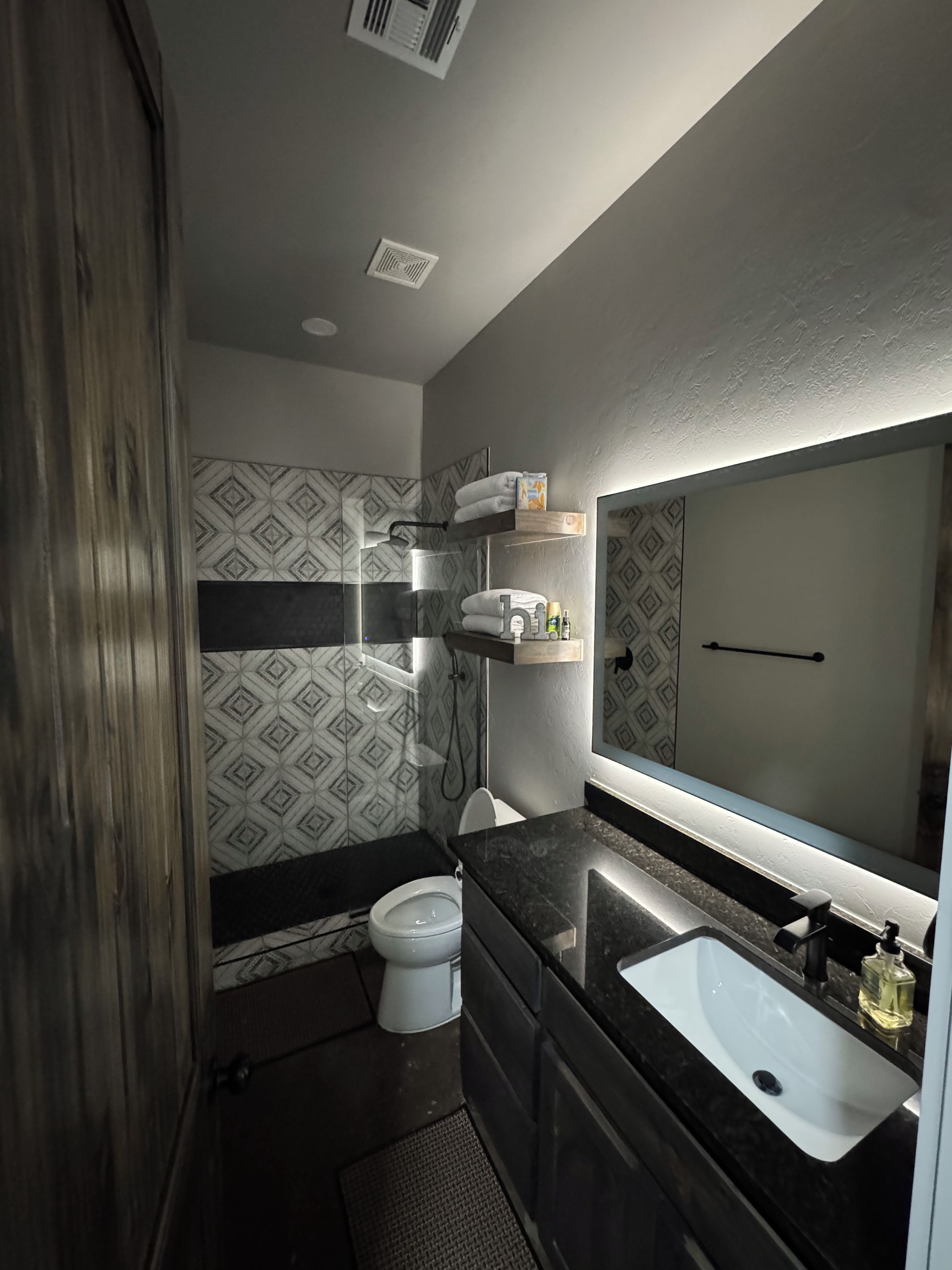 Une salle de bain moderne équipée d’une douche, de toilettes, d’un meuble-lavabo et d’un grand miroir.