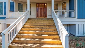 A wooden staircase leading to a porch with white railings and a double door. - Golf Course view secluded home in the heart of BHI (Bald Head Island)