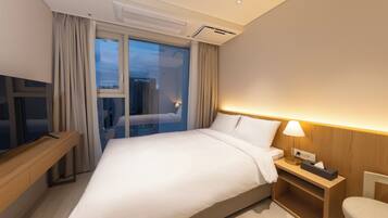 A hotel room with a large bed, a bedside table with a lamp, a TV on a wooden stand, and a window with curtains.