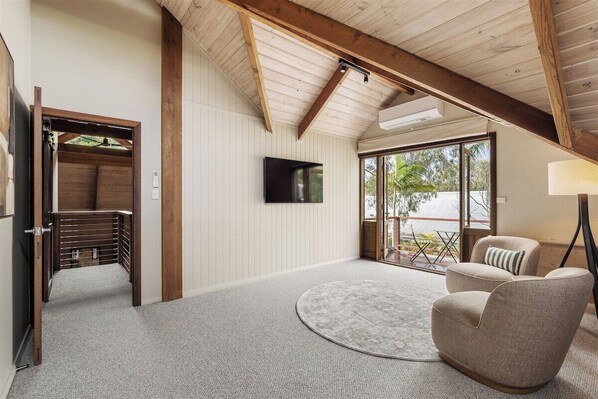 A modern interior with a high ceiling, a flat-screen TV mounted on the wall, a round rug, and two upholstered chairs.