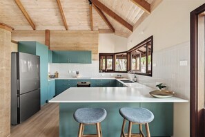Una cocina moderna con una isla central, vigas de madera en el techo y armarios color turquesa.