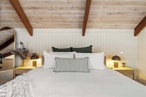 A bedroom with a wooden ceiling, a bed with white bedding, two bedside lamps, and a mirror on the wall.