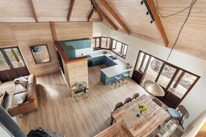 A modern interior with a kitchen, dining area, and living space, featuring wooden floors and large windows.