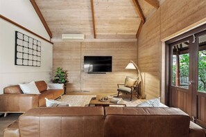 Un salon moderne avec un plafond en bois, un téléviseur à écran plat, un canapé, un fauteuil et une table basse.