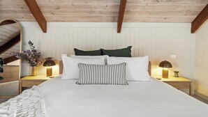 A bedroom with a wooden ceiling, a bed with white bedding, two bedside tables with lamps, and a mirror on the wall. - Pepperstone—Serene Coastal Hideaway with Fire Pit (Dunsborough)