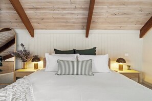 Une chambre avec un plafond en bois, un lit avec une literie blanche, deux tables de chevet avec des lampes et un miroir au mur.