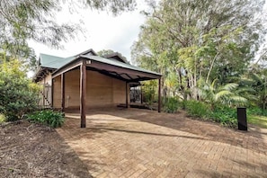 Ein Holzhaus mit einer Veranda, umgeben von Bäumen und einem Pflasterweg.