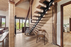 Un escalier avec des marches en bois et des rampes en métal, menant à un espace ouvert où se trouvent un banc et une chaise.