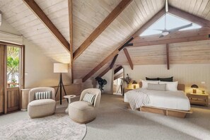 Ein Schlafzimmer mit einem großen Bett, zwei Sesseln, einem kleinen Tisch und einem Deckenventilator.