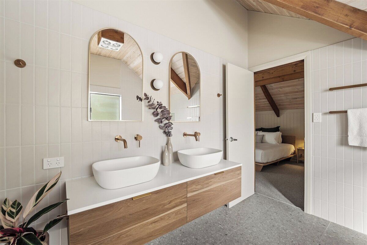 A modern bathroom with two sinks, wooden cabinetry, and a large mirror.