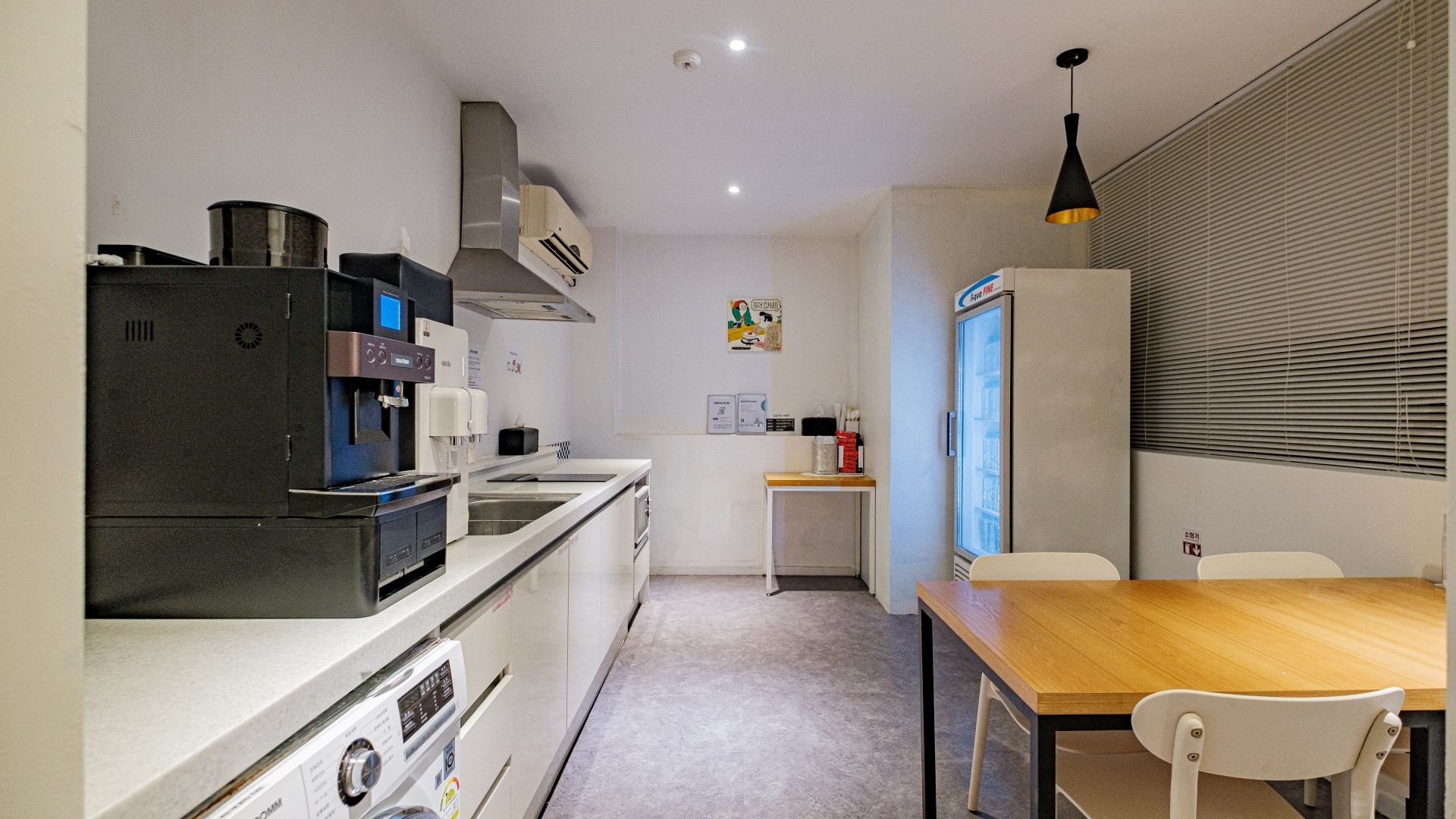 A compact kitchen with a coffee machine, a refrigerator, and a dining area with a table and chairs.