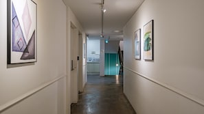 Un pasillo con obras enmarcadas en las paredes, un baño a la vista y una escalera que sube a otro piso.