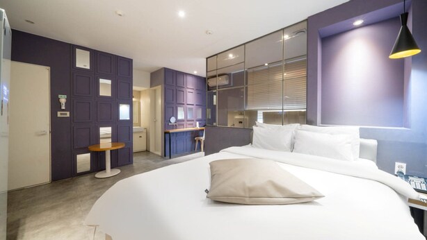 A modern hotel room with a large bed, a desk, and a bathroom visible through a glass partition. - NU Hotel (Cheonan)