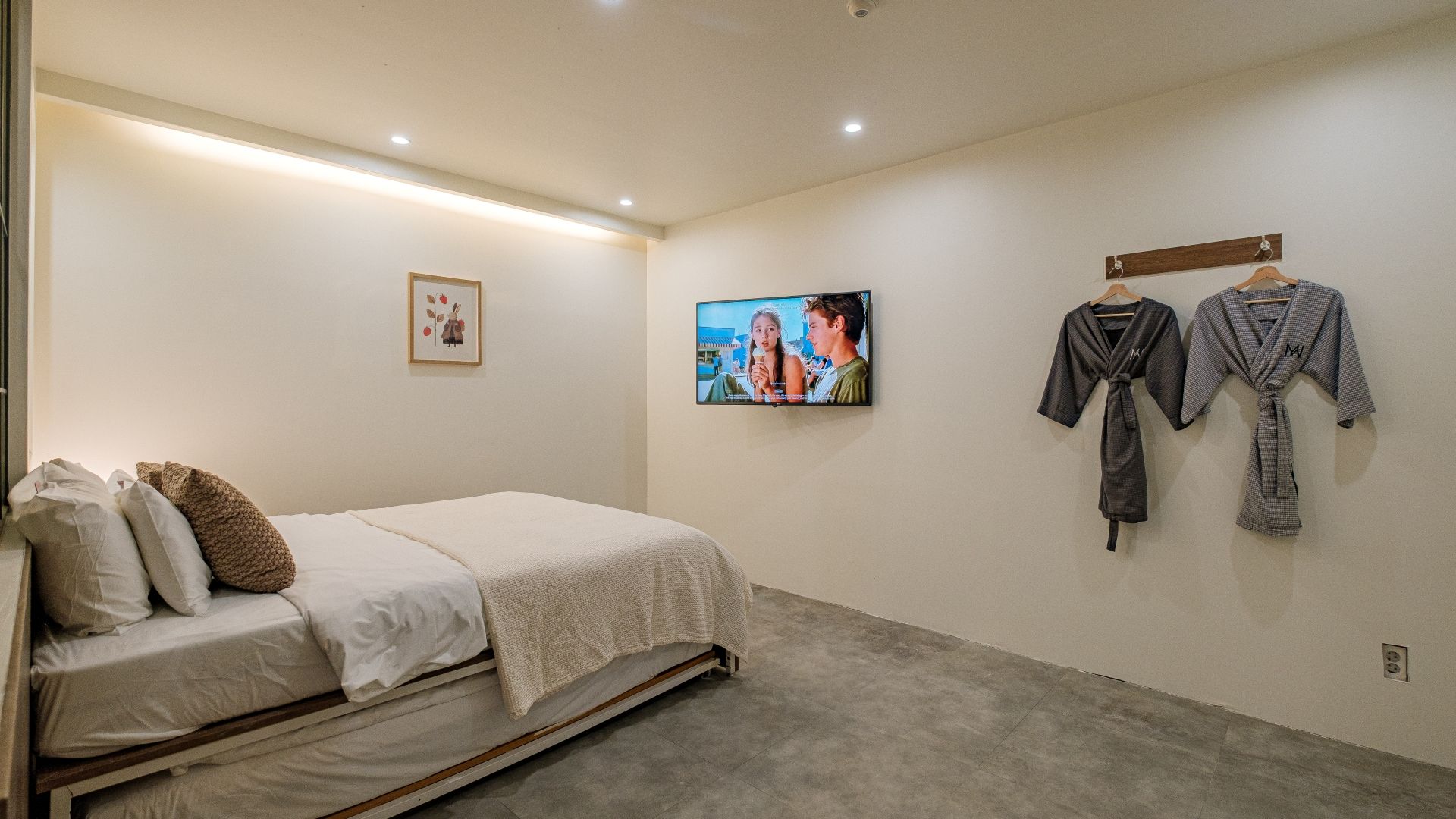 A bedroom with a bed, pillows, a TV, and two robes hanging on the wall.