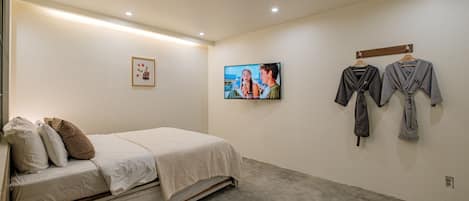 A bedroom with a bed, pillows, a TV, and two robes hanging on the wall.