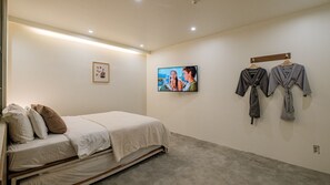 A bedroom with a bed, pillows, a TV, and two robes hanging on the wall. - NU Hotel (Cheonan)