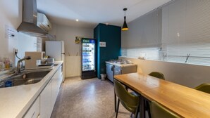 A compact kitchen with a sink, stove, and refrigerator, a small dining area with a table and chairs, and a vending machine. - NU Hotel (Cheonan)