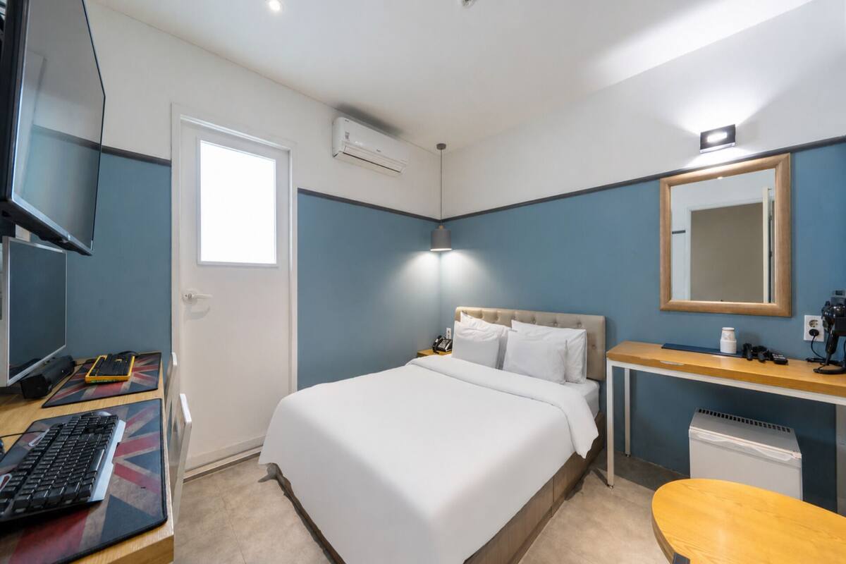 Ett hotellrum med en säng, ett skrivbord, en stol och ett litet bord med en lampa.