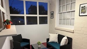 Ein Zimmer mit rotem Teppich, zwei schwarze Rattan-Sofas mit türkisblauen Kissen und einem Glastisch, sowie einem Topf mit Pflanze.