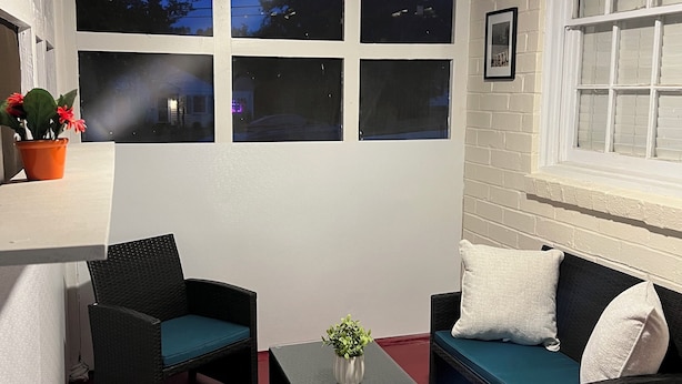 Ein Wintergarten mit Deckenventilator, einem schwarzen Couchtisch, zwei Korbstühlen, einer Couch mit türkisfarbenen Kissen und einem Blumentopf.