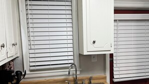 Eine Küche mit weißen Schränken, einer doppelten Spüle und einem Fenster mit Jalousien.