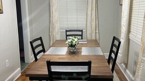 Ein Esszimmer mit Holztisch, vier Stühlen, einer Chandelieber und einer Blumenvase.