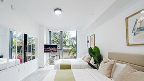 Habitación de hotel con dos camas, un ventanal grande, un televisor de pantalla plana y una planta verde.