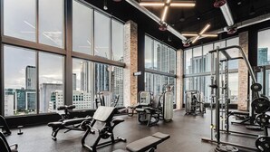 Un gimnasio con amplios ventanales, diverso equipo de ejercicio y vistas a la ciudad.